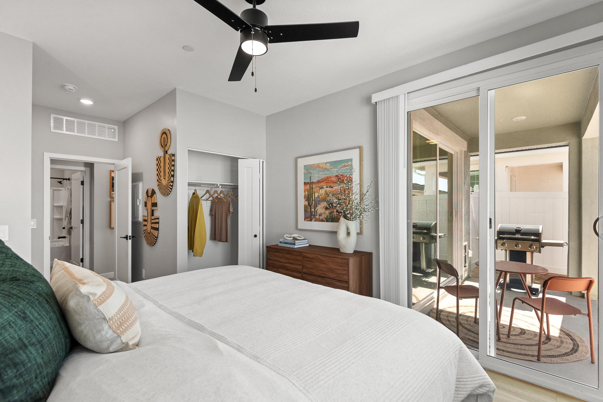 Origin modern bedroom with bed, open closet, dresser, and sliding door leading to a patio with a grill and chairs.