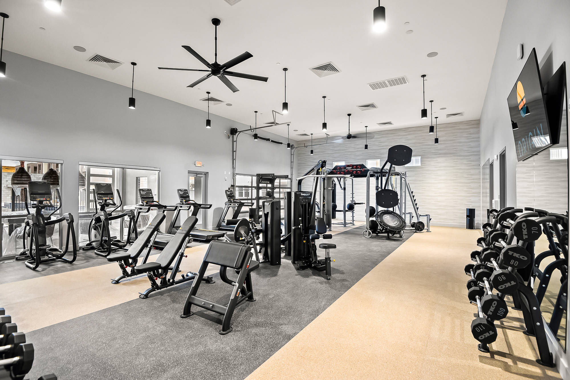 Modern gym with various exercise machines, free weights, and bright lighting in a spacious, clean room.