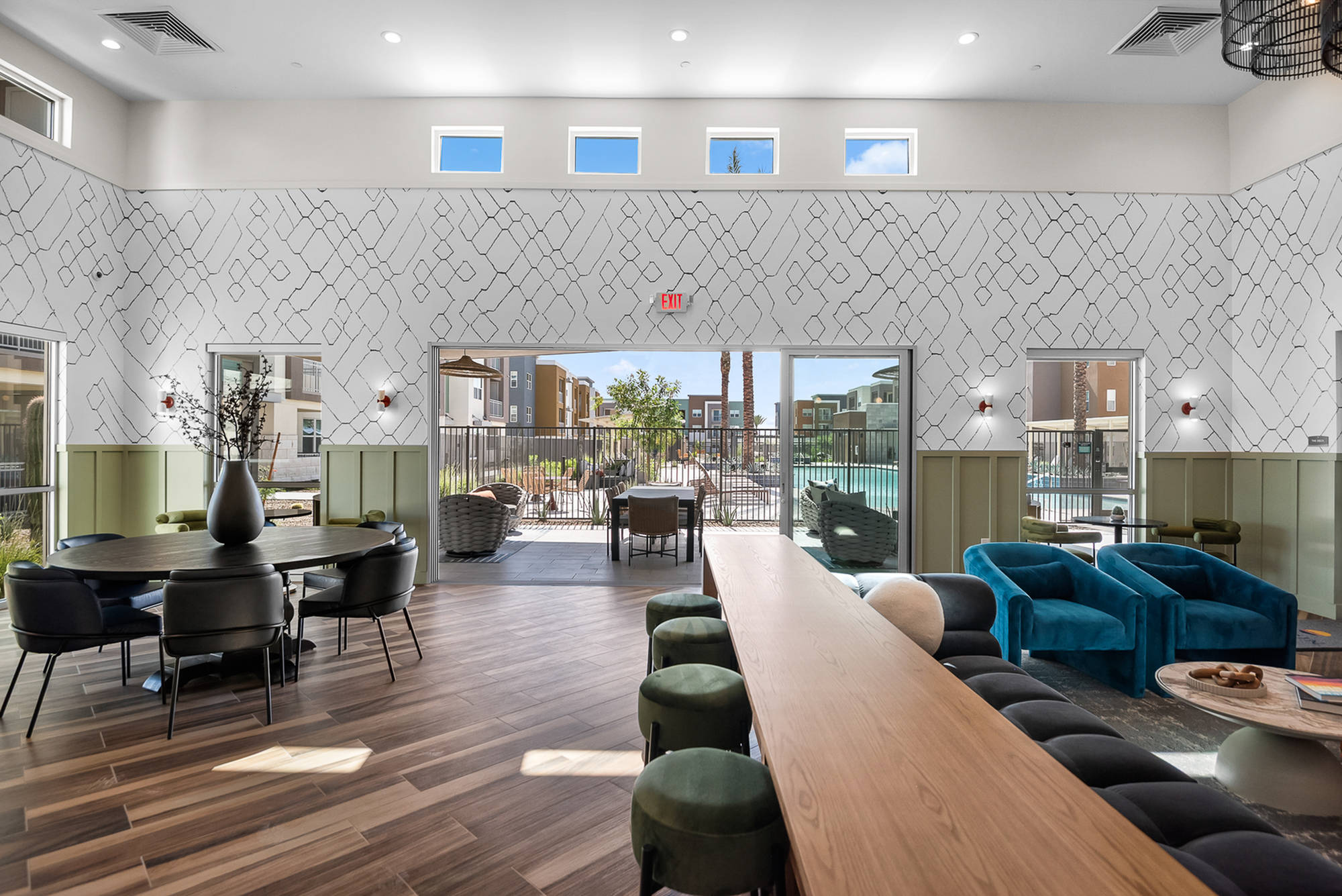 Modern lounge with large windows, stylish seating, wood floors, and a view of an outdoor pool area.