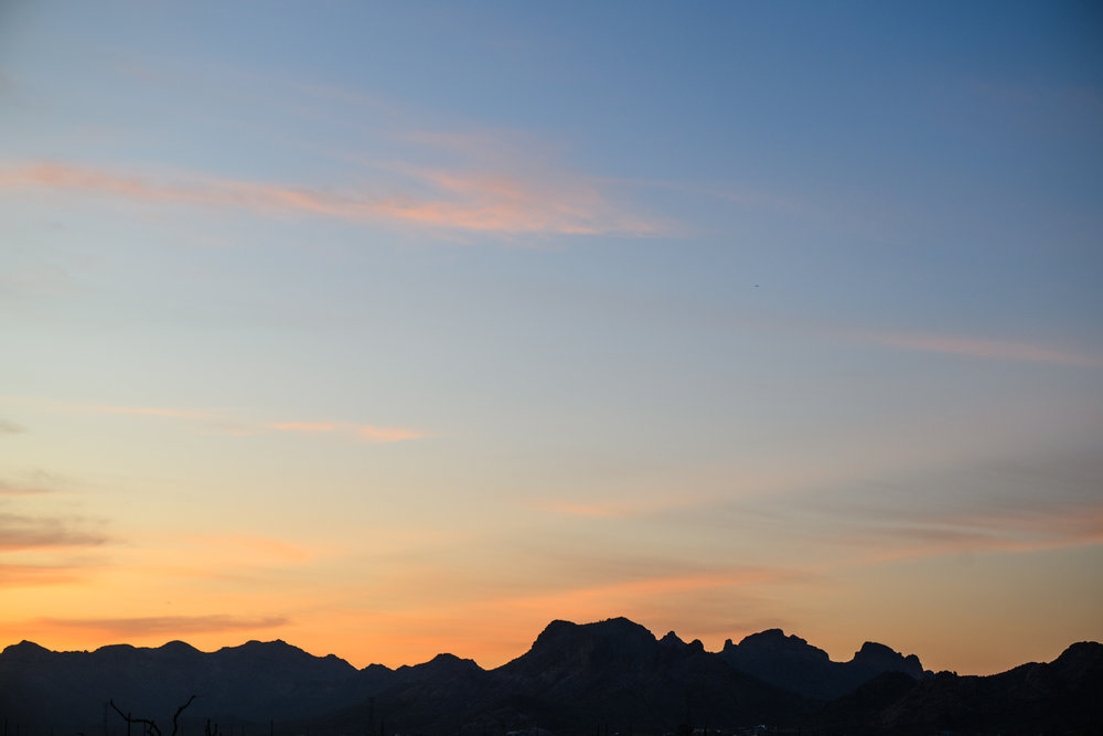 Silhouetted mountains beneath a colorful sunset sky with soft orange and blue hues.
