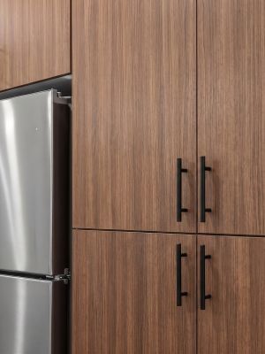 Stainless steel fridge and microwave next to brown wood cabinets with black handles in a kitchen.