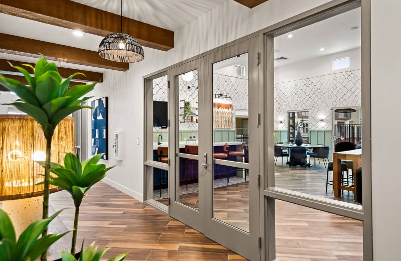 Modern lounge seen through glass double doors, featuring wood beams, stylish furniture, and decorative lighting.