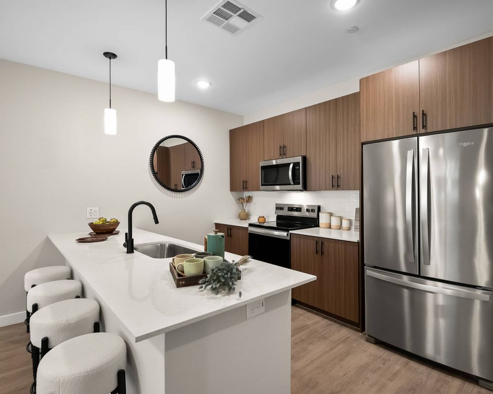 Modern kitchen with wood cabinets, stainless steel appliances, and a white island with three stools.