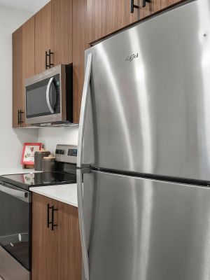 Modern kitchen with stainless steel fridge, microwave, oven, and wood cabinets with black handles.