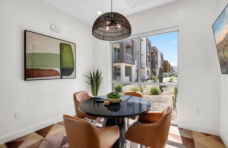 Modern dining area with four brown chairs, a round black table, art, a large window, and outdoor view.
